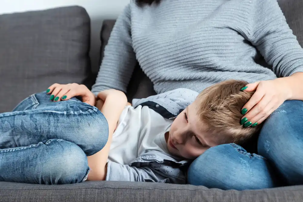 Chlapec leží na gauči s hlavou na klíně matky, drží si bolestivé břicho. Možný příznak zánětu slepého střeva.