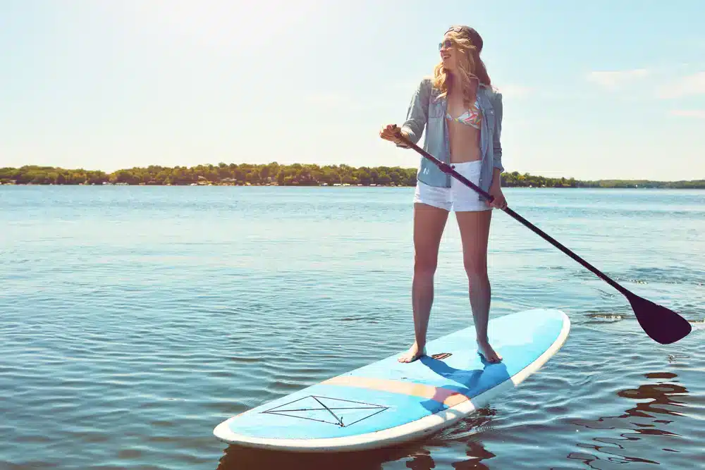 Žena stojící na paddleboardu s pádlem na klidné vodě, ideální pro rekreační paddleboarding.