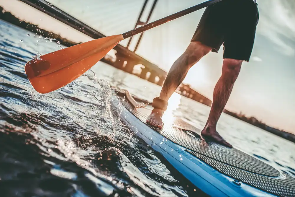 Detailní záběr pádla a nohou na paddleboardu, zachycení dynamiky při jízdě.