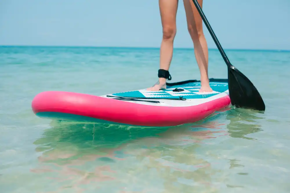 Žena stojící na paddleboardu s růžovým pruhem na moři, ukázka univerzálního allround paddleboardu.