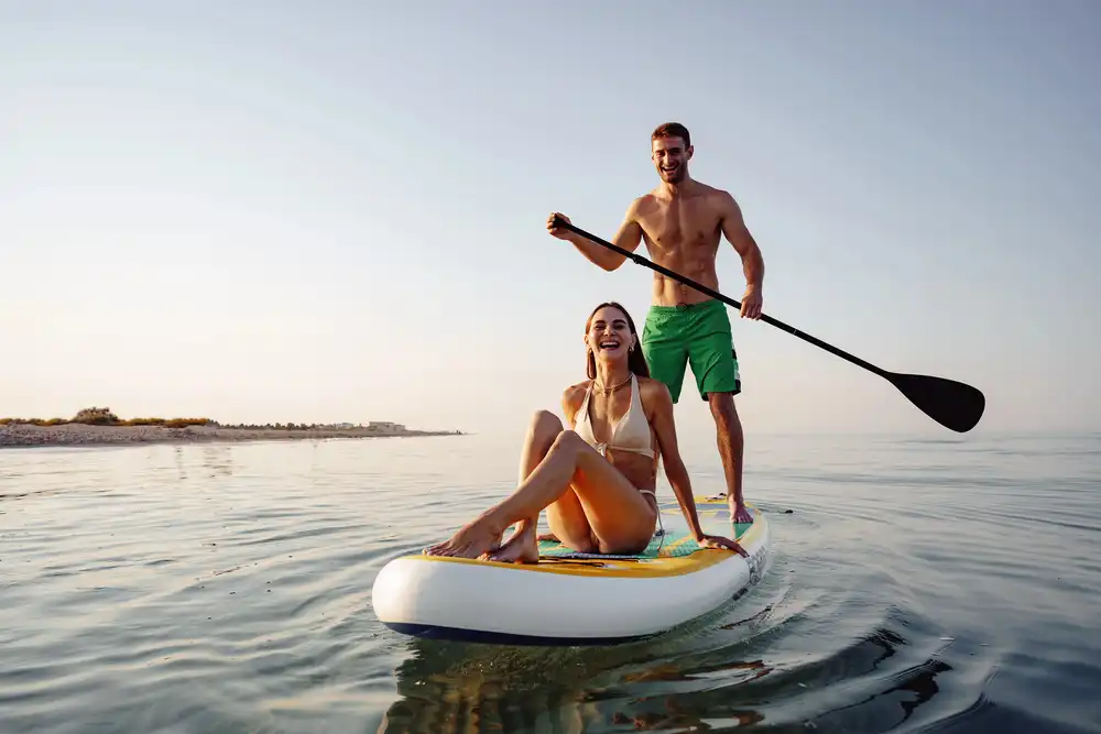 Pár na paddleboardu, muž pádluje a žena sedí, vhodné pro společné dobrodružství.