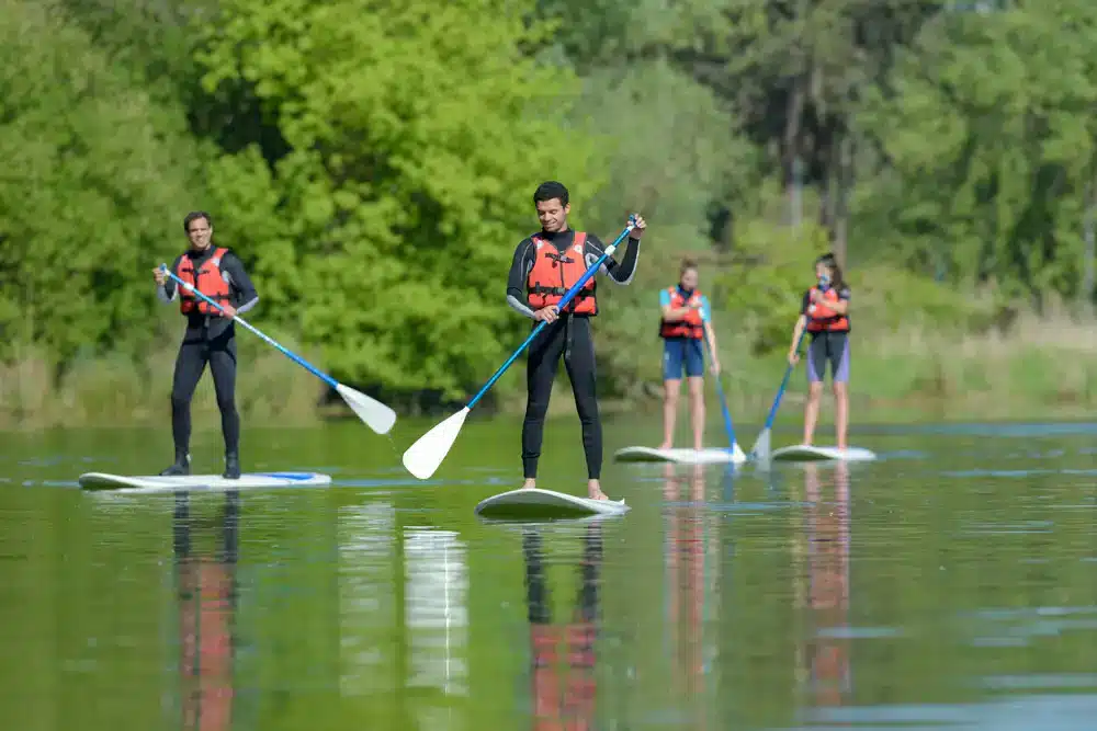 Skupina lidí na paddleboardech na klidné řece, příklad touring paddleboardů pro delší trasy.