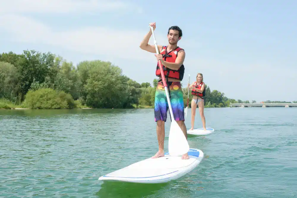 Muž a žena na paddleboardech s pádly na klidné řece, vhodné pro rodinné výlety.