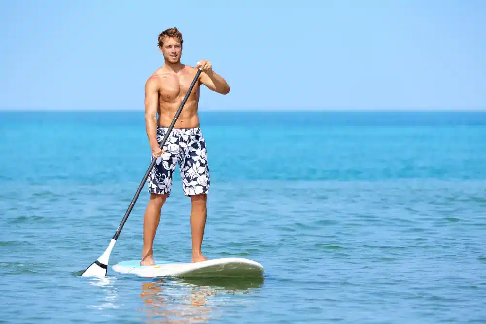 Muž pádlující na paddleboardu v moři, vhodné pro sportovní i rekreační využití.