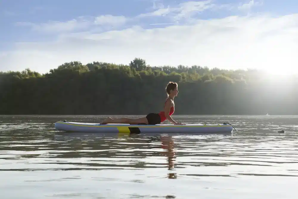 Žena cvičící jógu na paddleboardu při východu slunce, paddleboardy vhodné pro jógu.